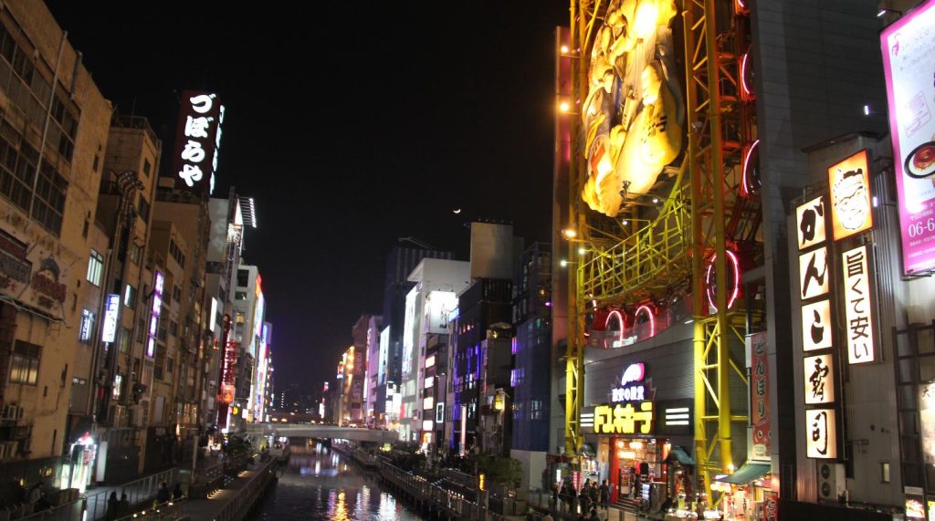 Illuminated signs and the Ebisu Tower Ferris wheel reflected in the Dotonbori canal at night